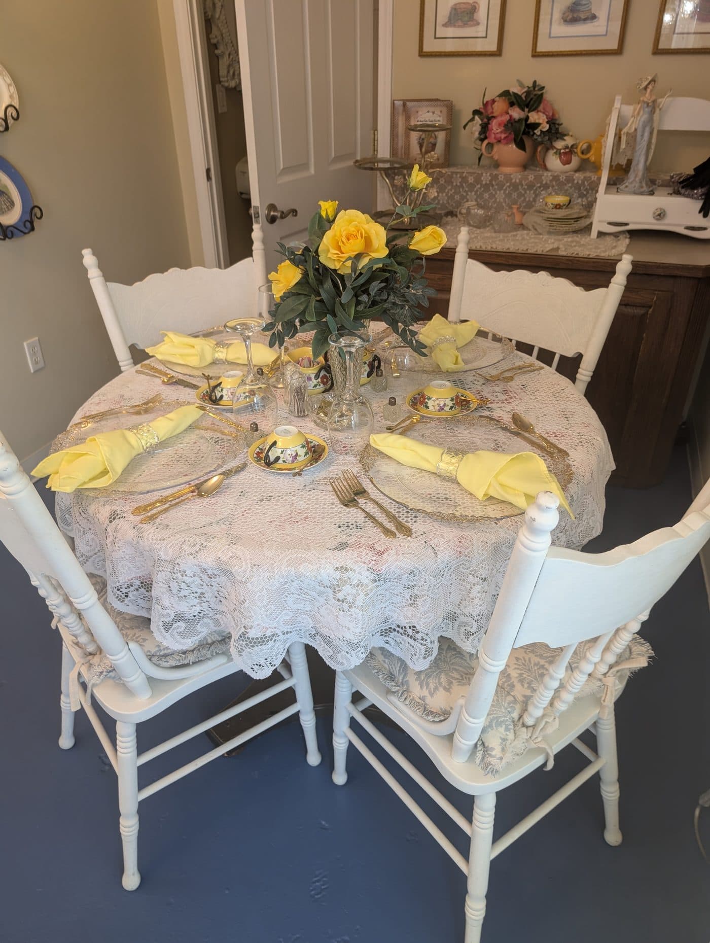 A round table laid with lace, gold flatware, yellow napkins and mixed china