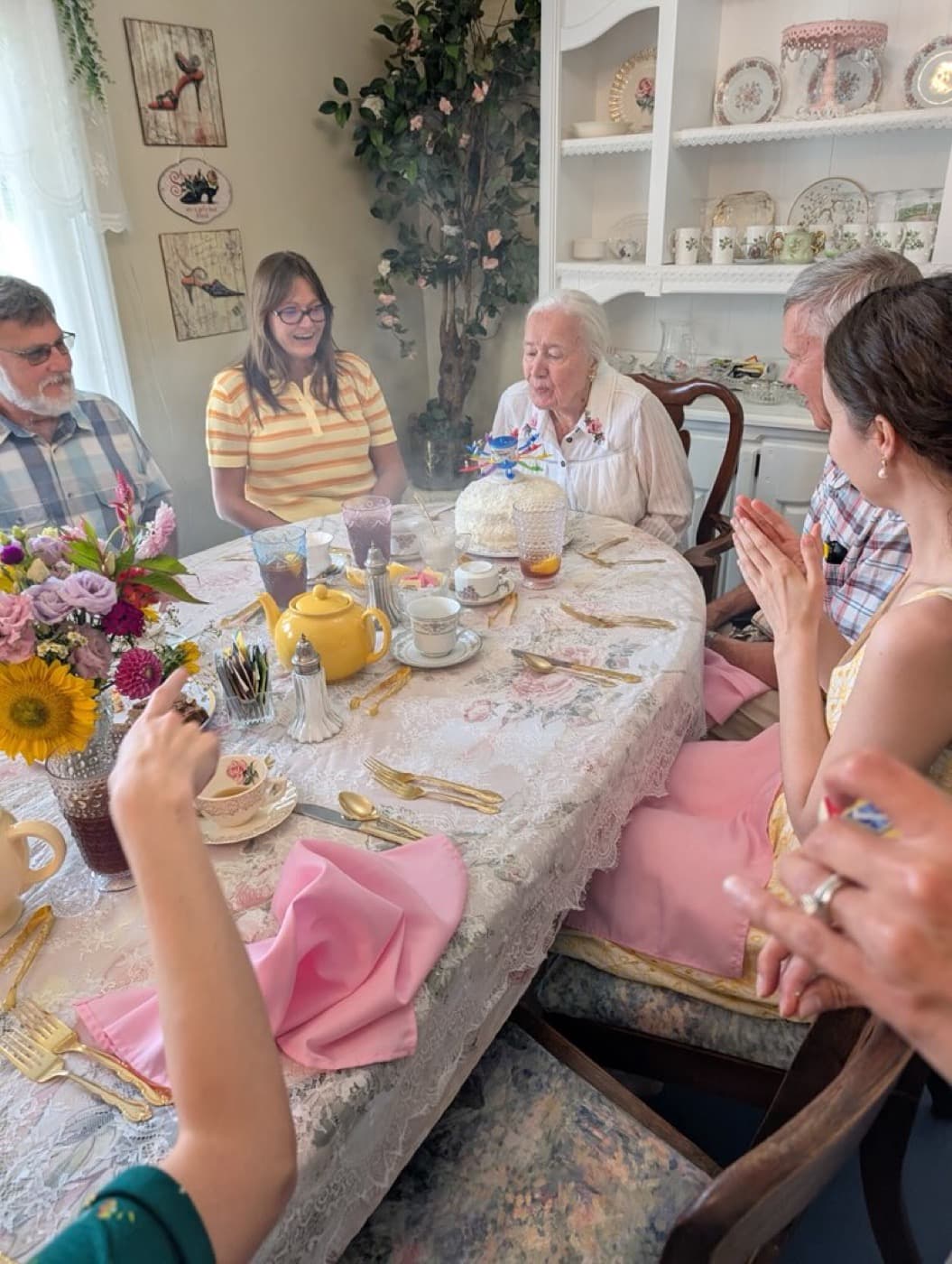 A birthday cake with its candles lit, guests looking on