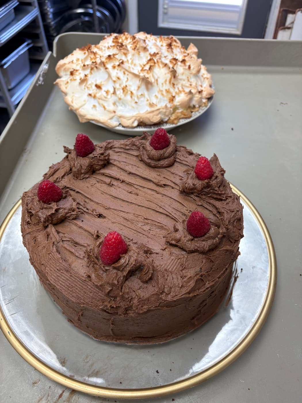A chocolate raspberry layer cake beside a tall meringue pie