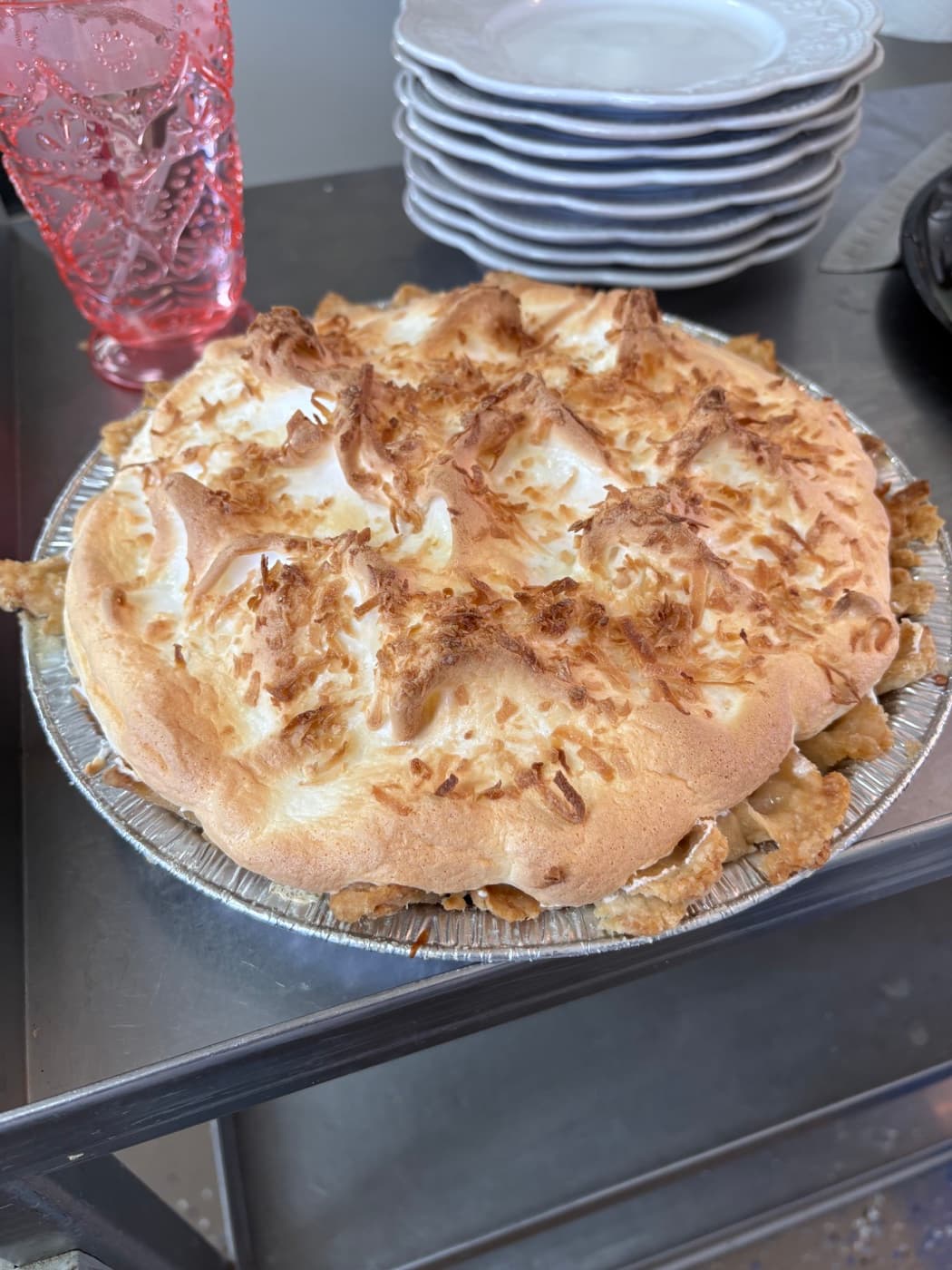 A coconut meringue pie, peaked and toasted, beside a stack of plates