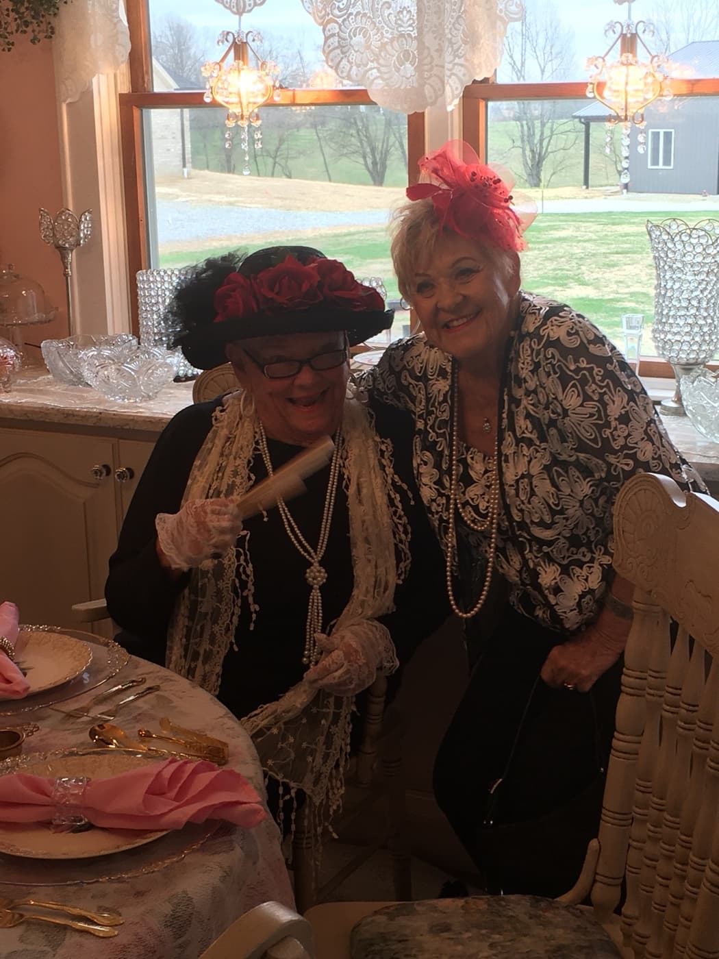 Ruth King and another guest in hats and pearls, laughing together at the table
